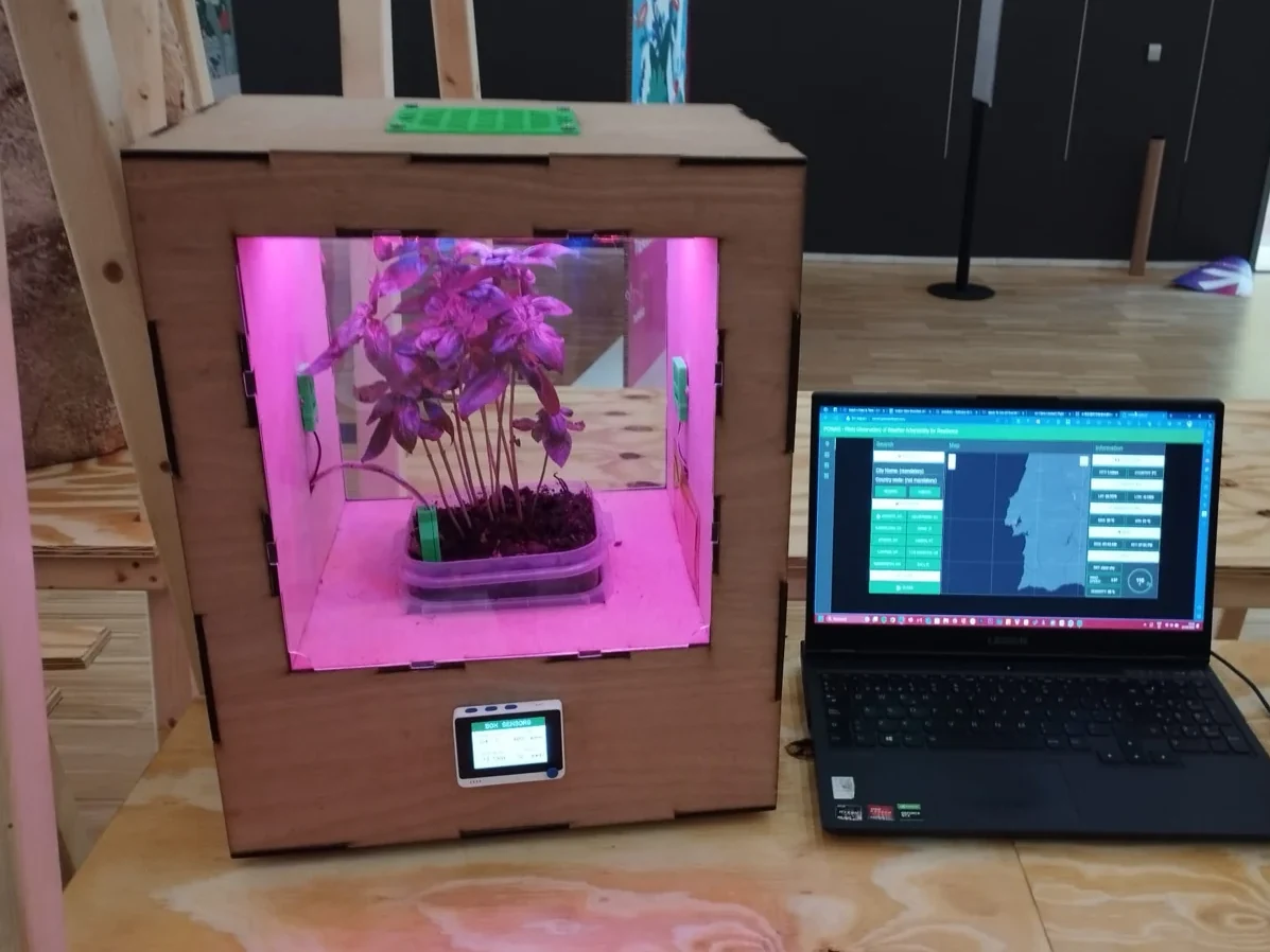 POWAR CS simulator with basil under grow lights, next to a laptop showing the platform, at Fixing the Futures (2023)